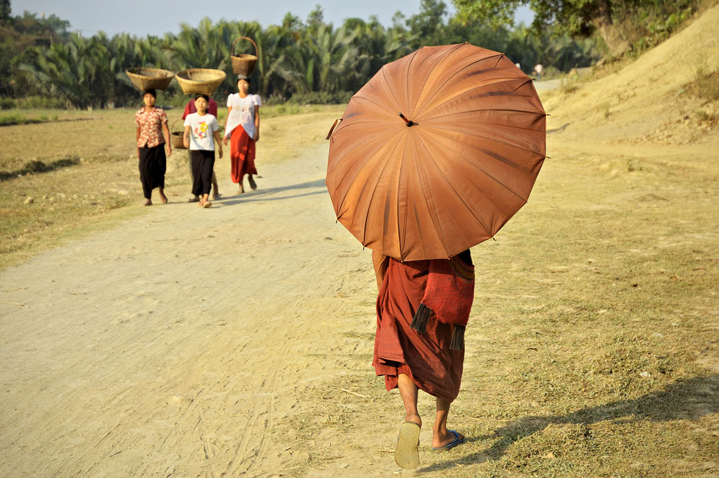 Moine et femmes marchant sur une route poussiéreuse à Mrauk U