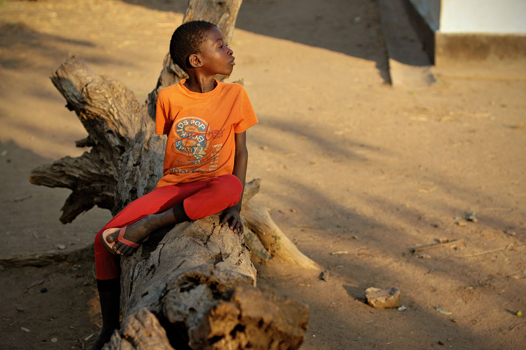 Jeune garçon assis sur un tronc d'arbre dans le village de Kawaza