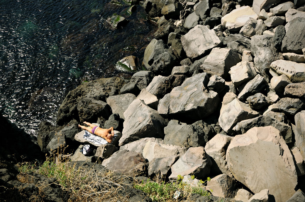 Homme qui bronze sur les rochers de Santa Maria la Scala en Sicile