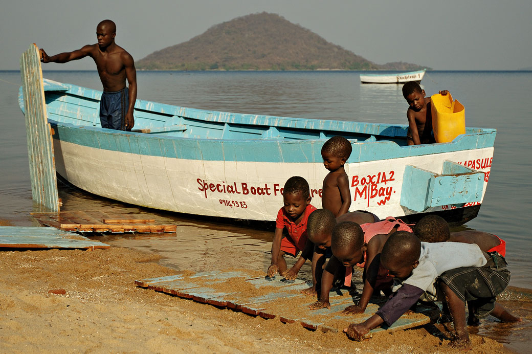 Homme qui nettoie son bateau avec des enfants à Cape Maclear