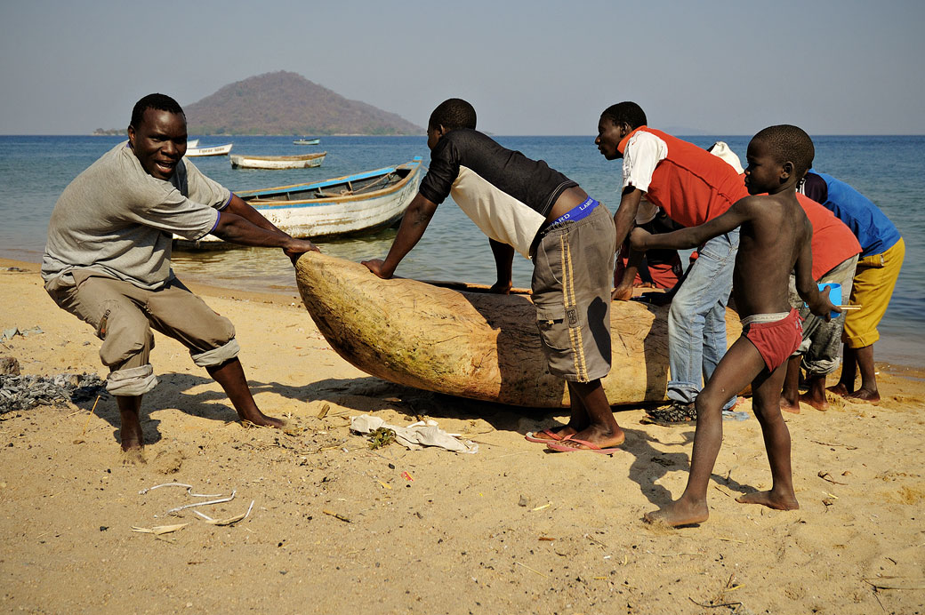 Hommes qui tirent une pirogue sur la plage à Cape Maclear, Malawi