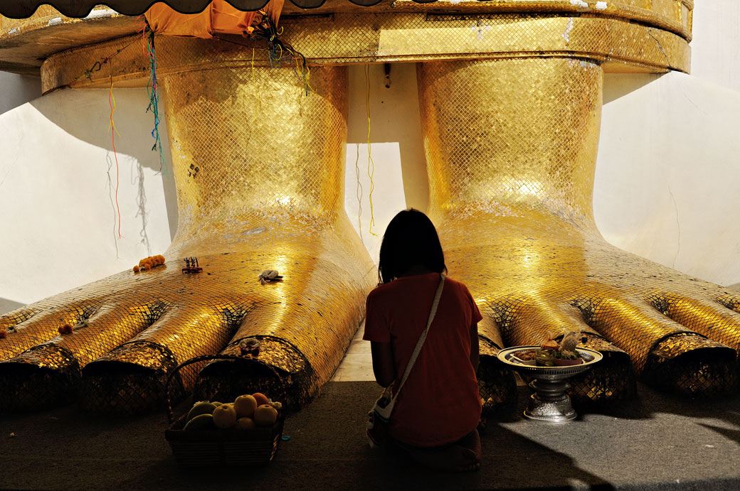 Femme qui médite au pied du Bouddha de Wat Intharawihan à Bangkok